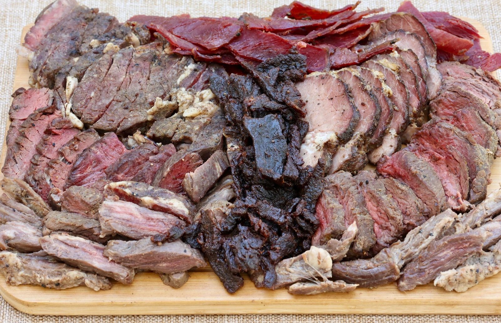 Sliced steak and candied pastrami piled on a wooden board