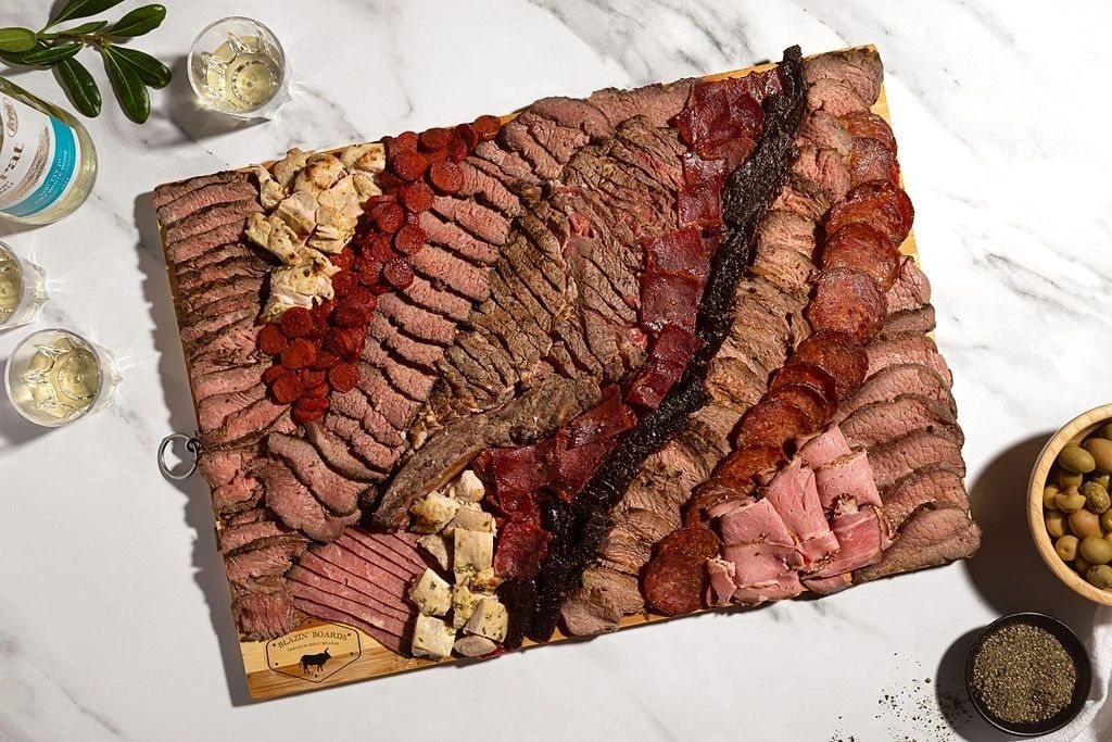 A square board of sliced meats and salami rounds, with pistachios and olives