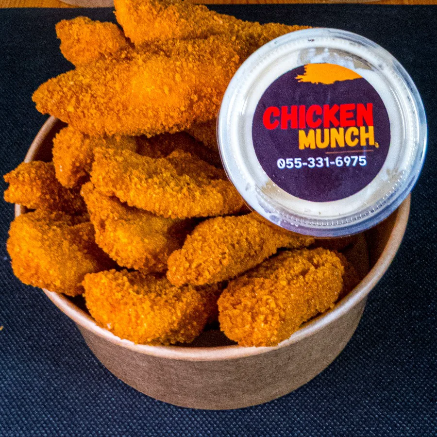 Shnitzel Bites, breaded chicken fingers in a kraft bowl with a Chicken Munch sauce pot