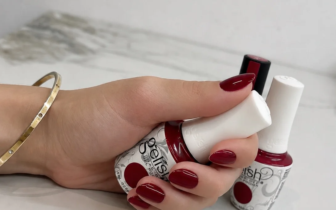 A hand holding two bottles of ruby red gel polish, with ruby red gel nails