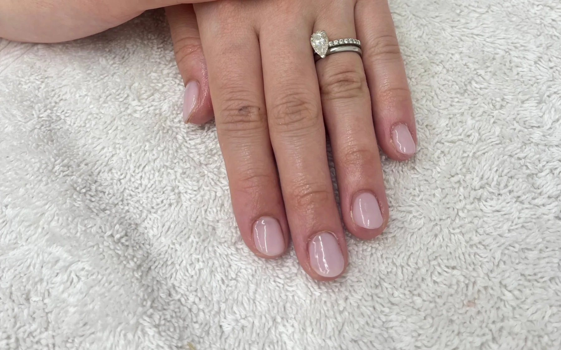 Pale pink gel nails on a client, hands on a towel