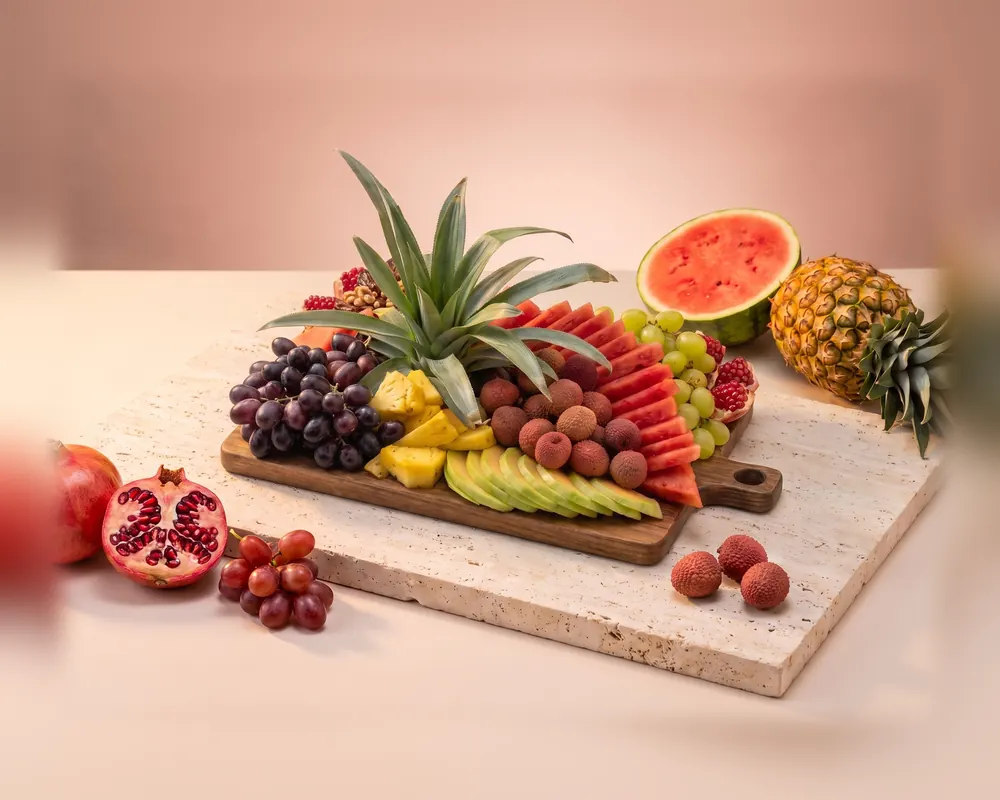The Medium platter: a wooden board with a pineapple crown, dark grapes, lychees, watermelon, melon and pomegranate