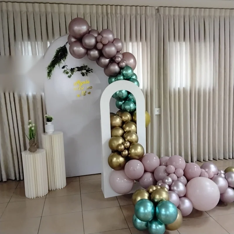 עמדת צילום של מיכל בלונס: קשת בלונים ורודה, ירוקה וזהובה סביב קשת לבנה עם הקדשה אישית ועמודים עם עציצים