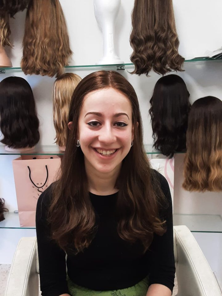 A client in the salon chair in a long brown wig, smiling