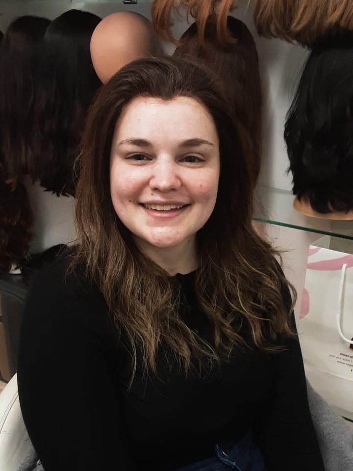 A client in the salon chair, long dark wig, the wig shelves behind her