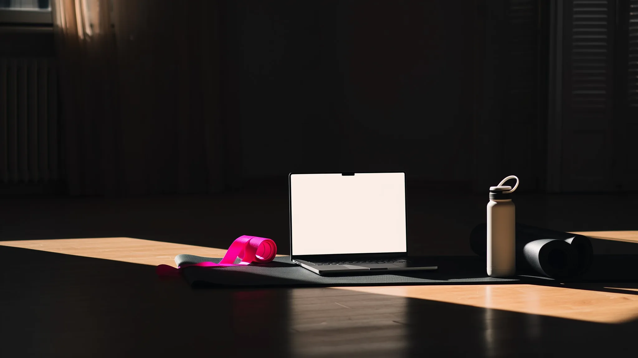 A laptop beside a yoga mat and a pink resistance band