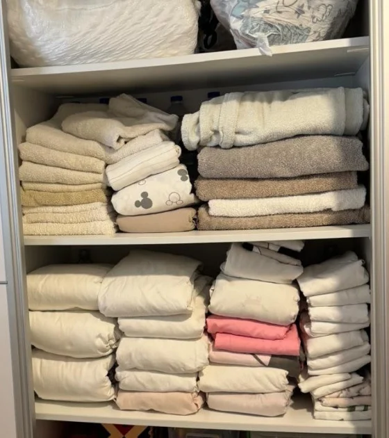 A linen cupboard with towels and bedding stacked unevenly