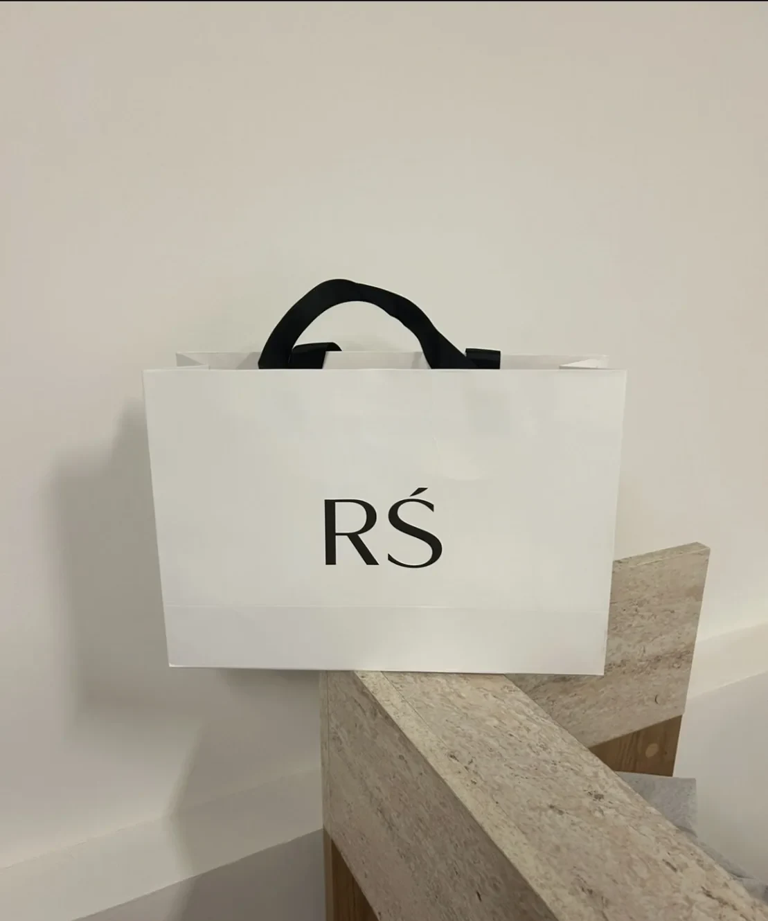 The white RS shopping bag with black ribbon handles
