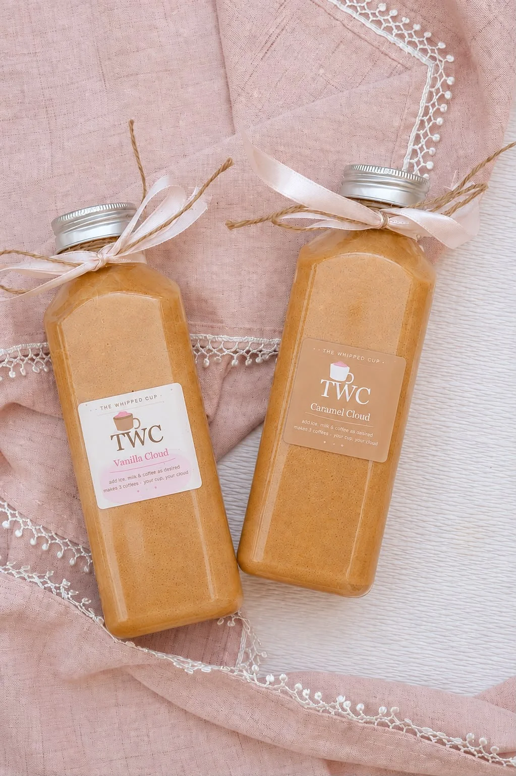 Two jars of The Whipped Cup tied with ribbon on pink linen