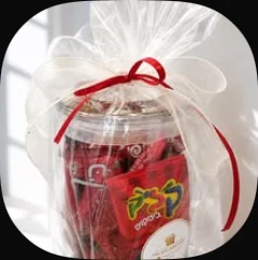 A glass cookie jar of sweets wrapped in cellophane with a red ribbon