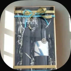 An electric bottle opener and a bottle in a gold-edged box tied with a blue ribbon