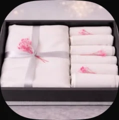 A white tablecloth and napkins with pink embroidery in a black box