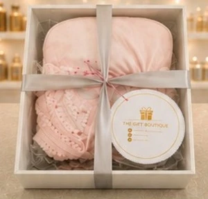 A soft pink knitted set in a clear box, tied with a silver ribbon